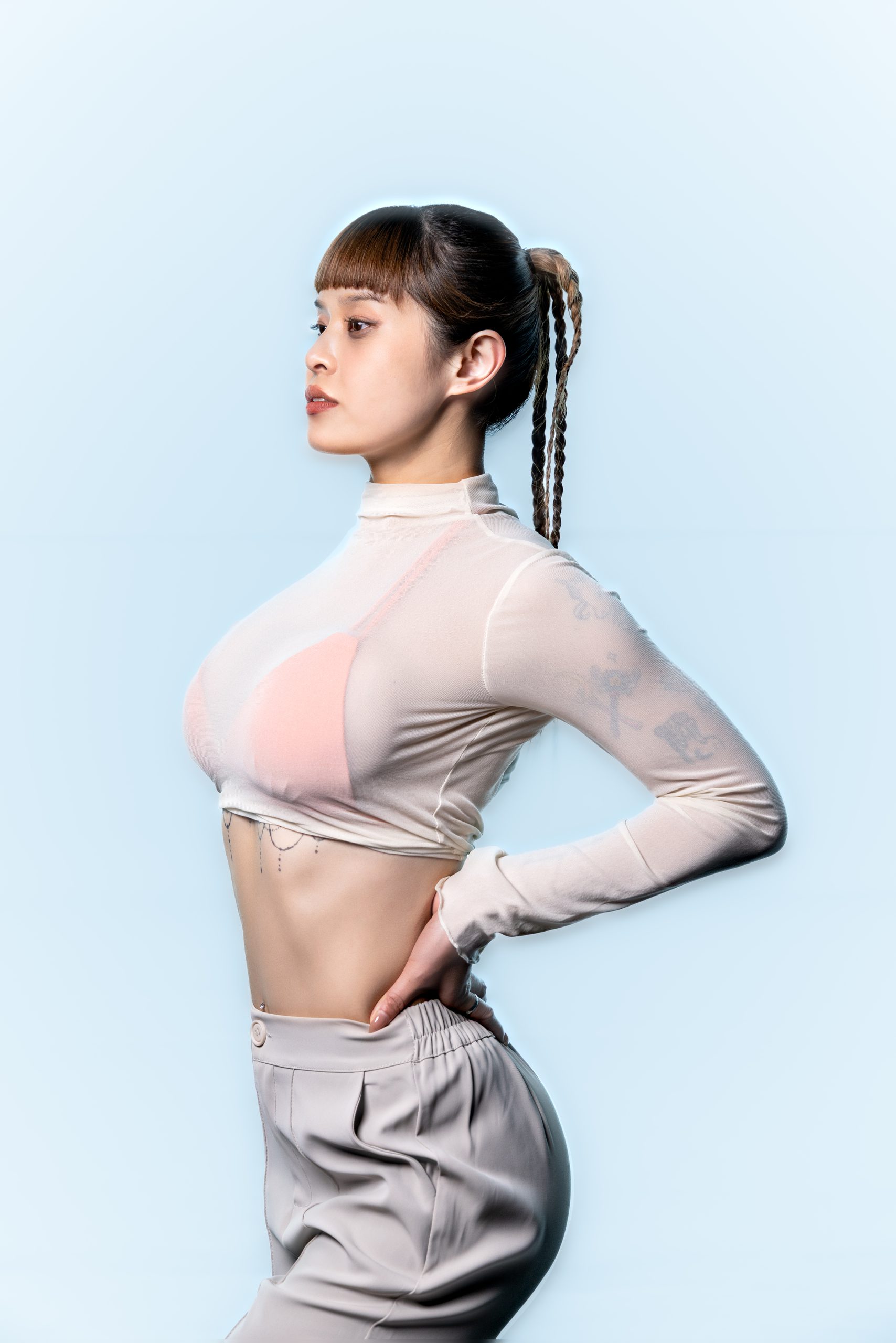 淺藍背景前的灰粉色套裝人像，站姿一手插腰，光線明亮均勻。