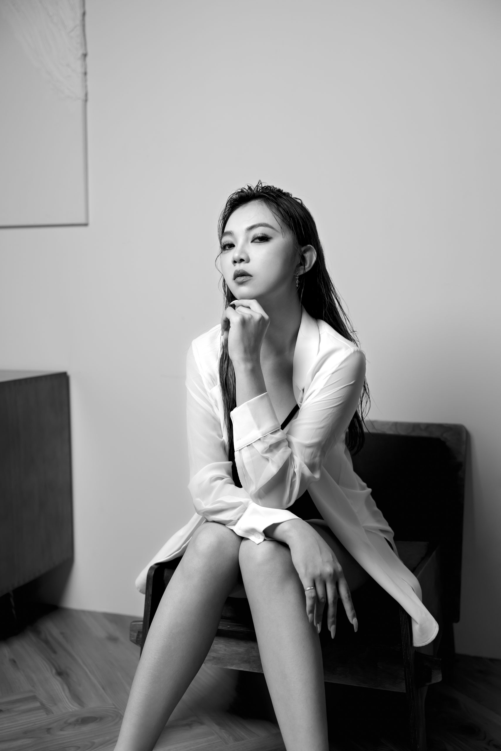 白襯衫造型的黑白坐姿人像，模特兒單手托腮，光線集中於臉部。